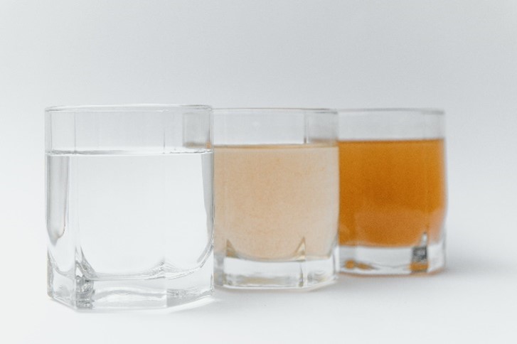 An image of several glasses of well water, the first is rusty in color from iron, and the last is clear thanks to Reynolds Water Conditioning.